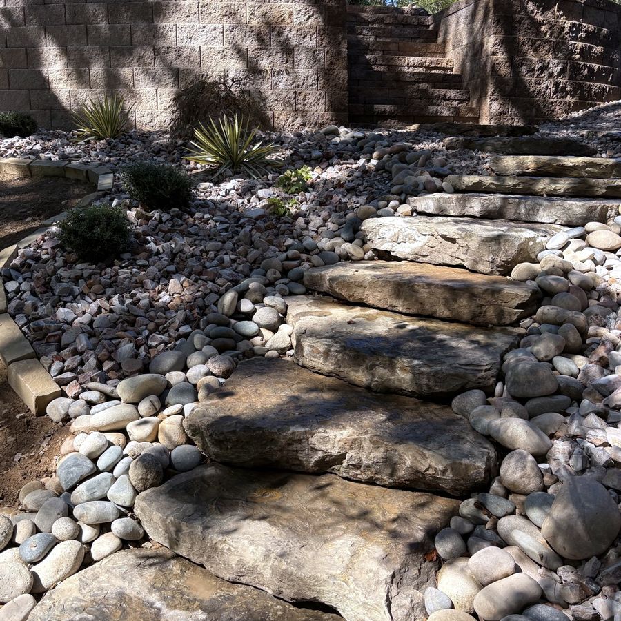 Stacked boulder steps climbing through a river rock bed to a block wall, built by the Amanda's Villa hardscape team