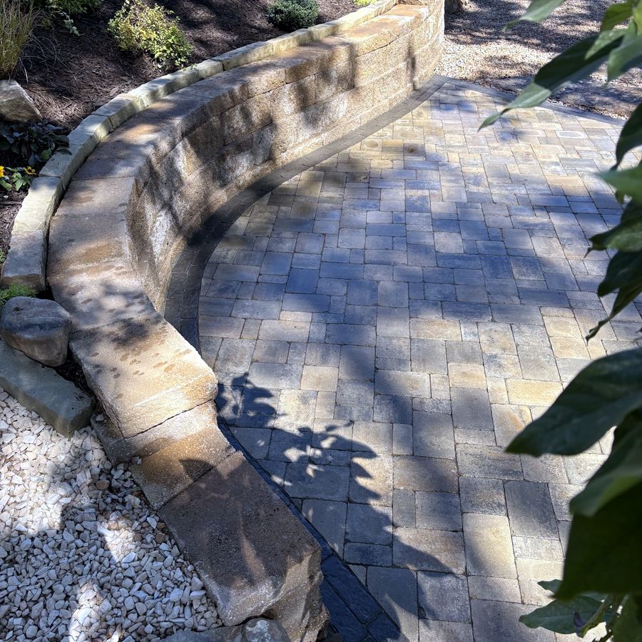 A curved block retaining wall wrapping a gray paver patio, built by the Amanda's Villa hardscape team