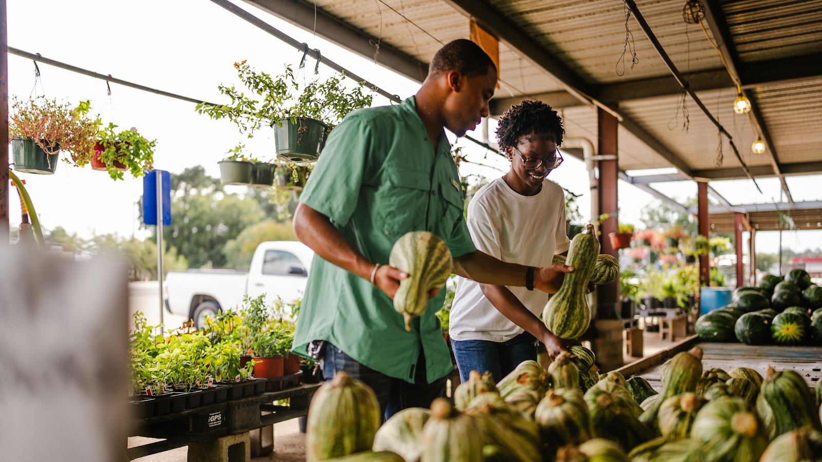A smiling couple choosing squash at a covered produce stand