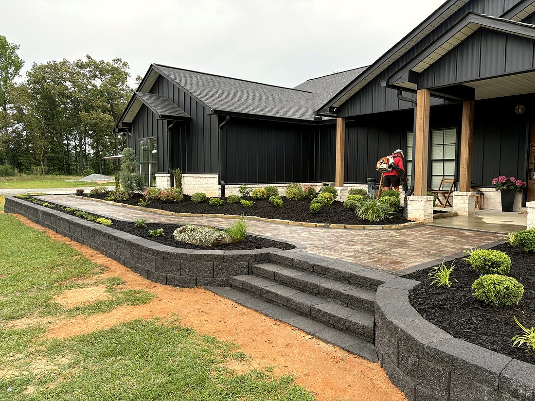 A raised paver walk with block retaining walls, wide steps and new planting beds in front of a dark farmhouse, built and planted by Amanda's Villa