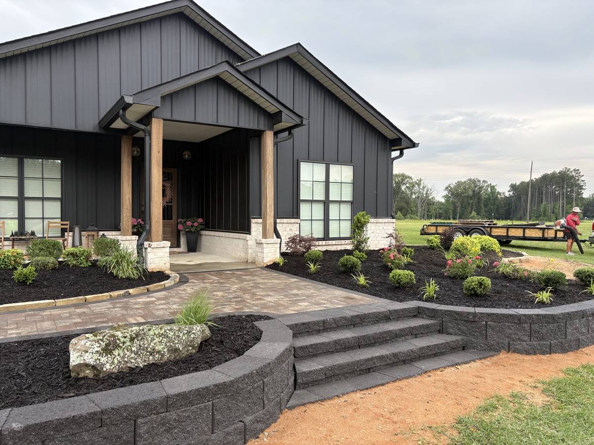 Block retaining walls, wide paver steps and new beds across the front of a dark farmhouse