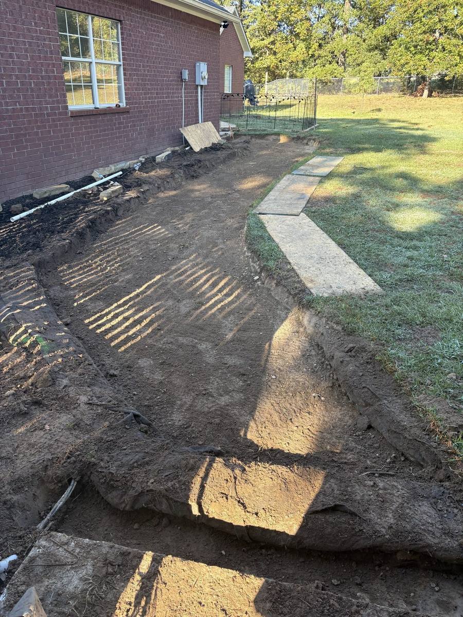 Ground dug out along the side of a brick house during a hardscape job