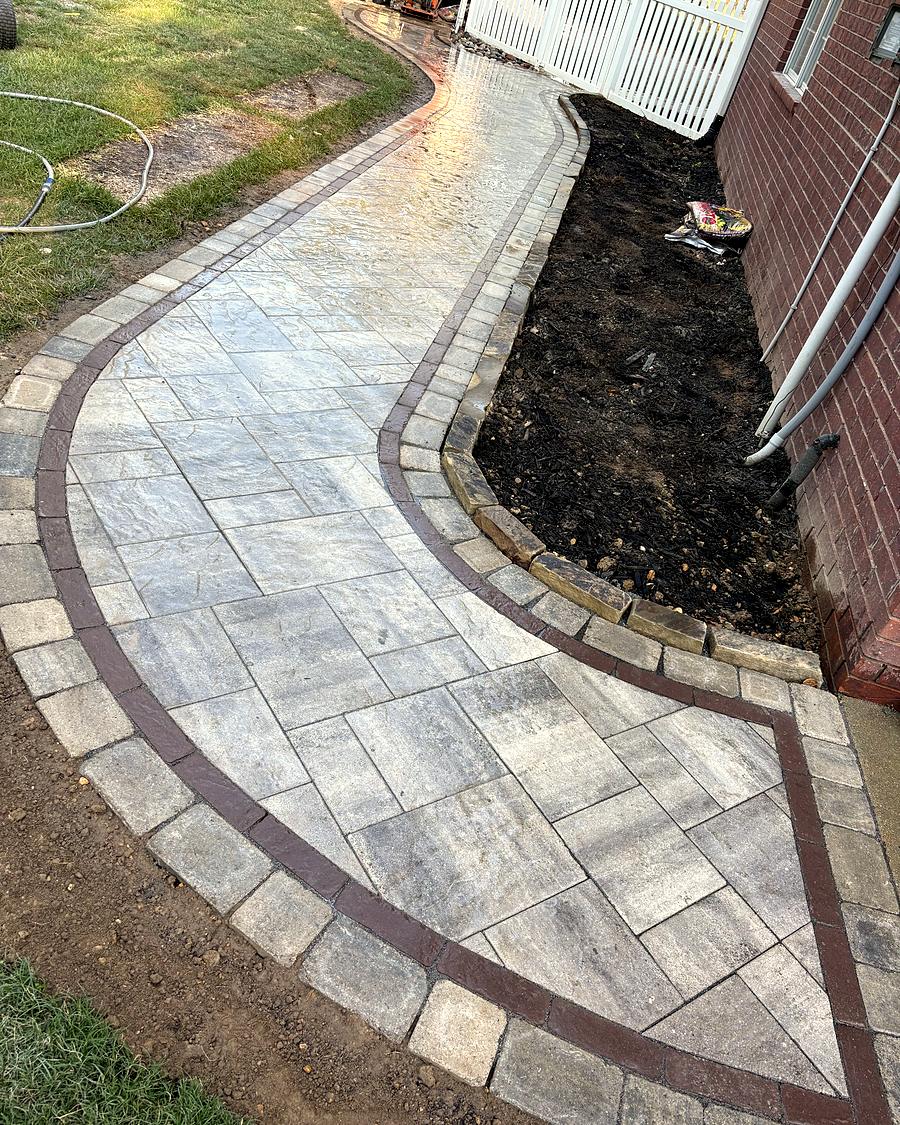 A curved gray paver path along a brick wall, built by Amanda's Villa