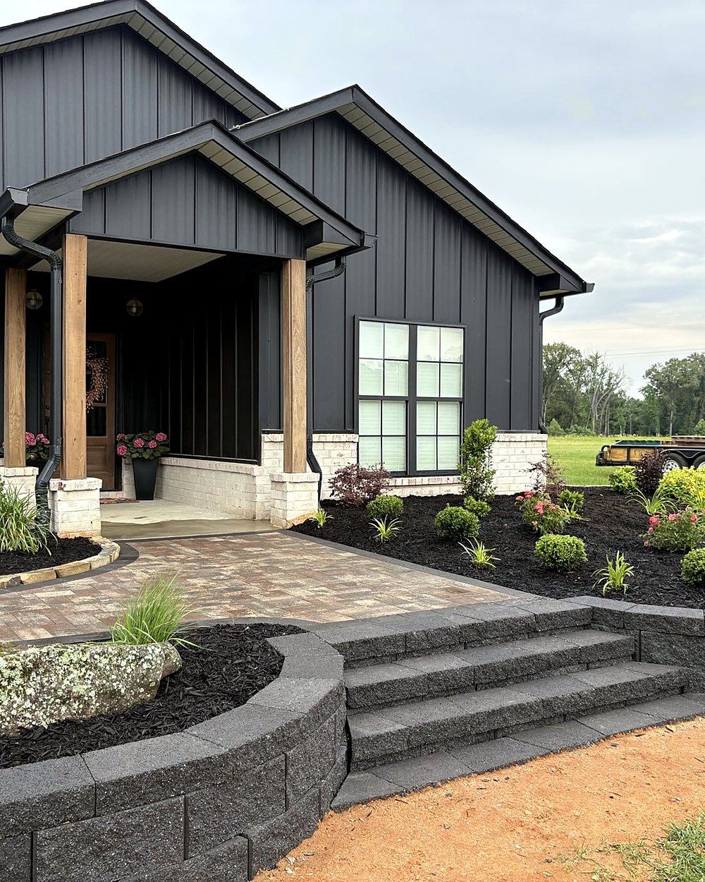A paver walk, block retaining walls and wide steps leading to a black farmhouse porch, built by Amanda's Villa