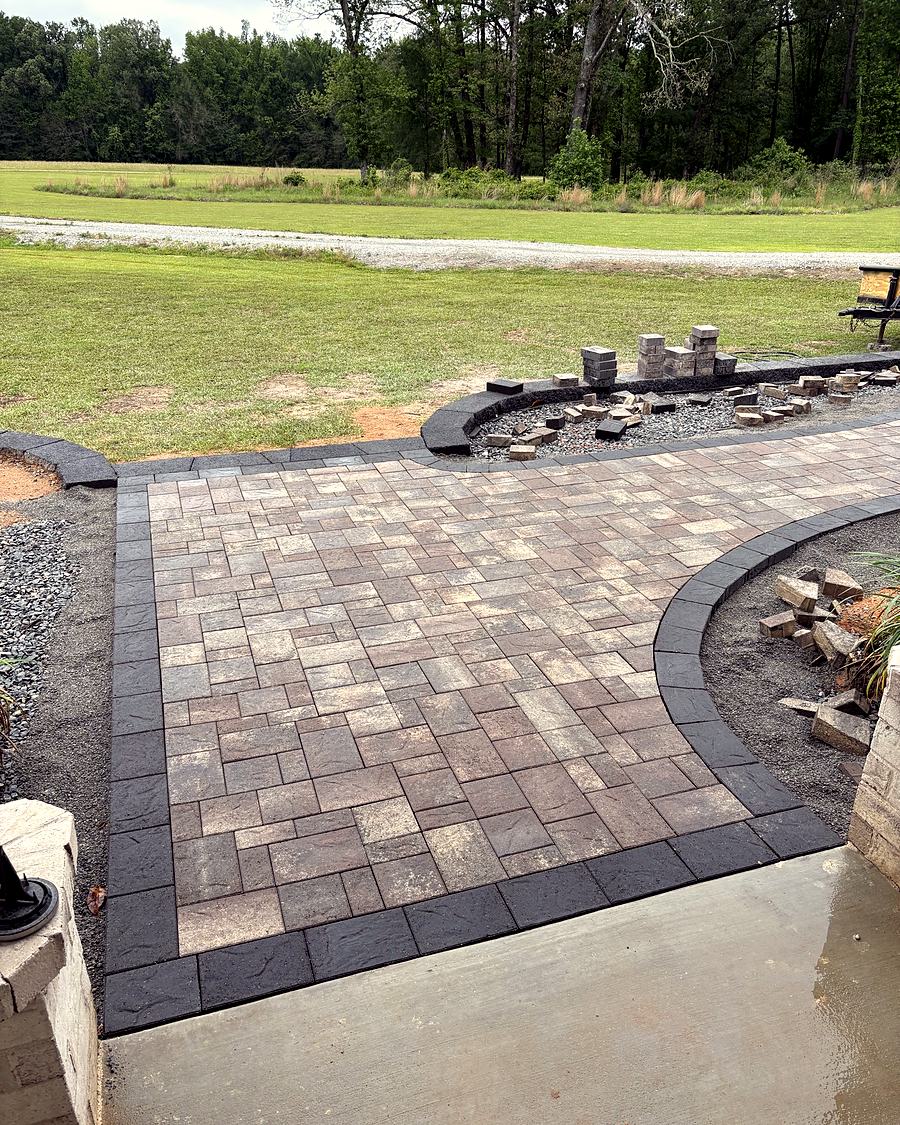 A paver patio with a charcoal border and a curved planting bed, built by Amanda's Villa