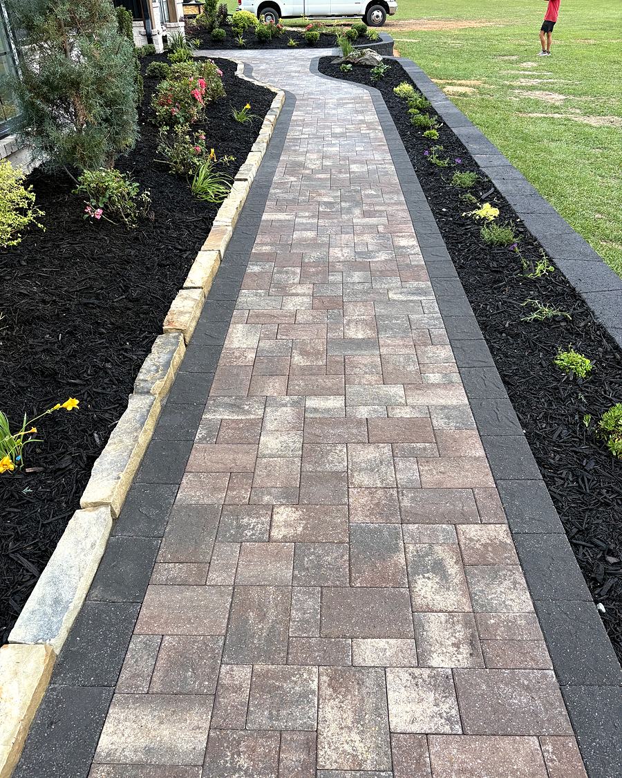 A long, straight paver walkway with a charcoal border between new beds