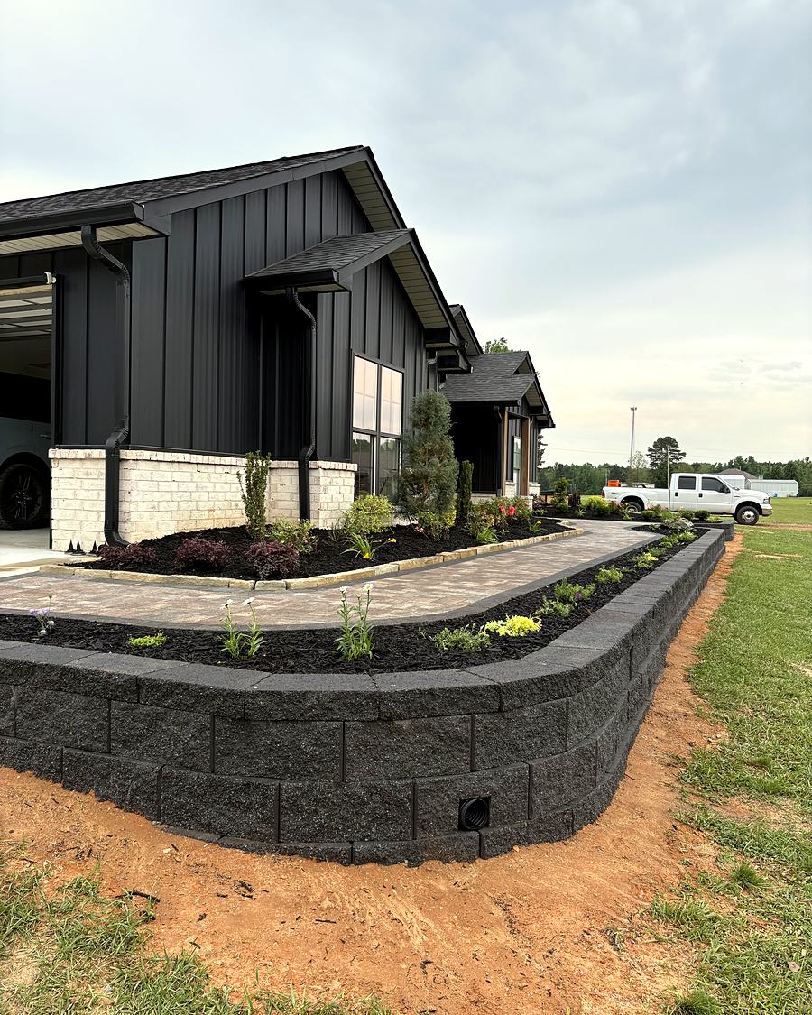 A block retaining wall holding a raised planting bed beside a farmhouse