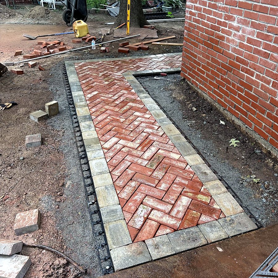 Herringbone brick pavers being set on a compacted base with border pavers in place