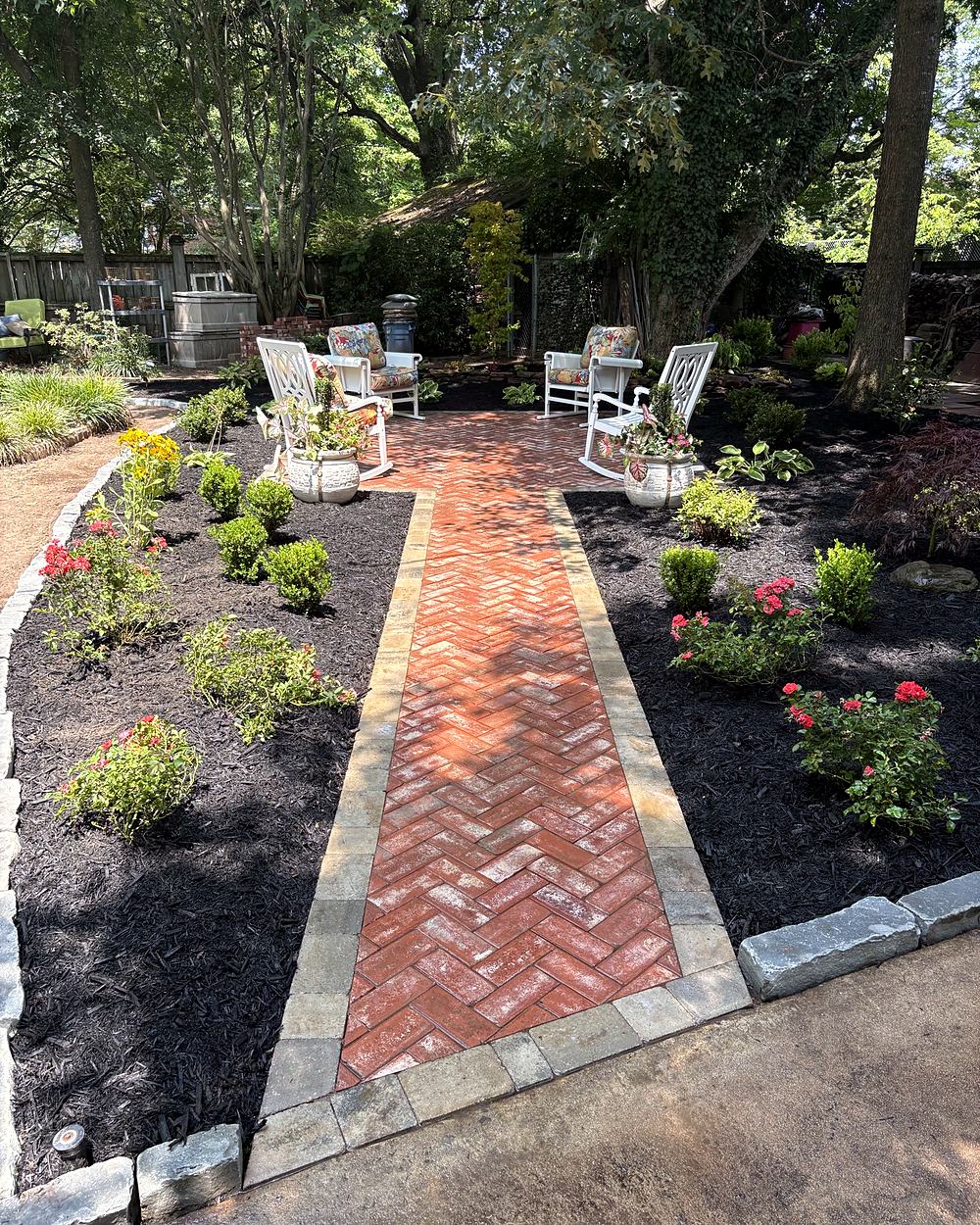A herringbone brick path through new garden beds to a patio with white chairs
