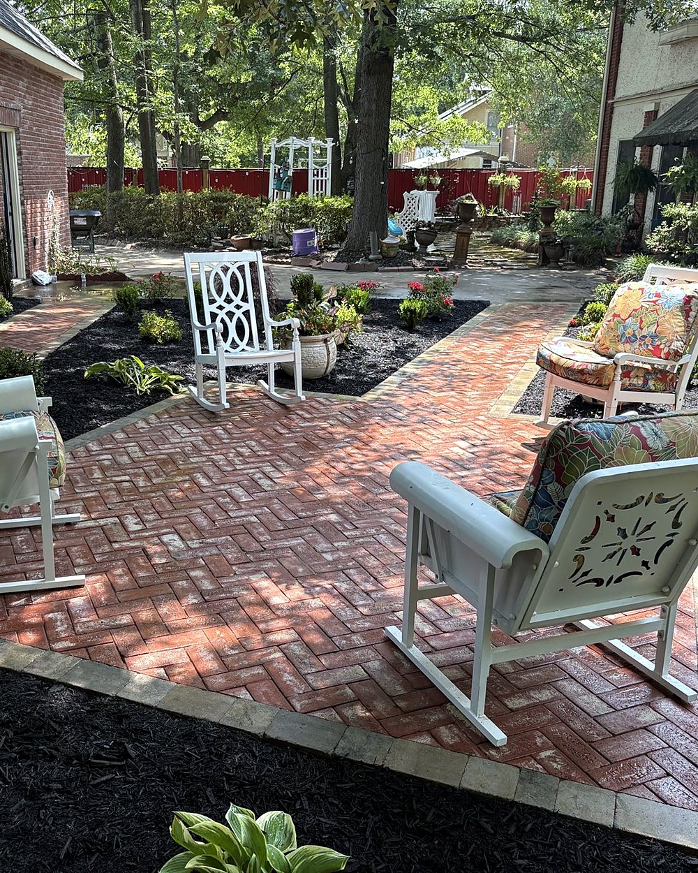 A herringbone brick patio with white rocking chairs and new planting beds, built by Amanda's Villa