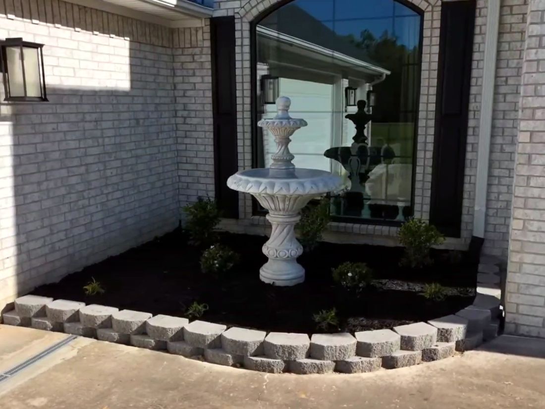 After: A mulched bed with a fountain, small shrubs and a stone block border.