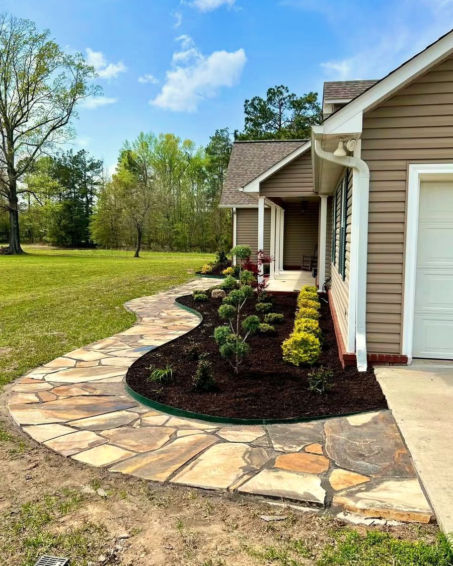 A new bed of shrubs with steel edging beside a flagstone walk along a house
