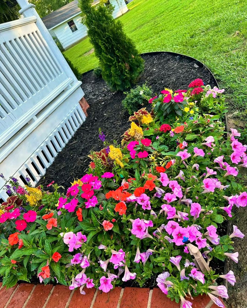A curved flower bed of pink and red impatiens and petunias beside white porch steps, planted by Amanda's Villa
