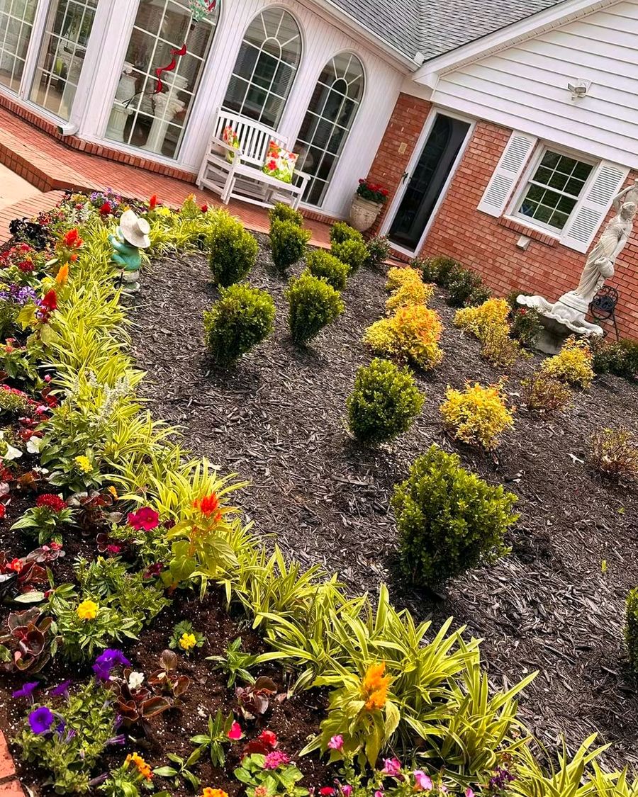 A planted bed of shrubs and annuals along a brick house, designed by Amanda's Villa