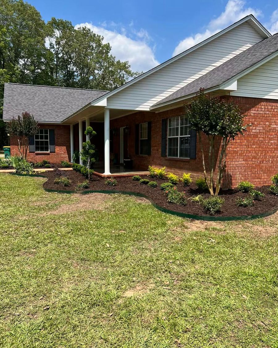 New beds of shrubs and a crape myrtle along the porch of a brick house