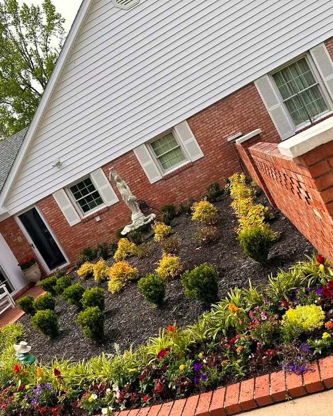 A freshly mulched bed of shrubs and flowers beside a brick wall