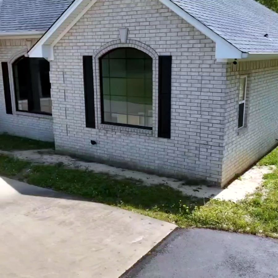 The bare corner of a white brick house beside the driveway before any work began