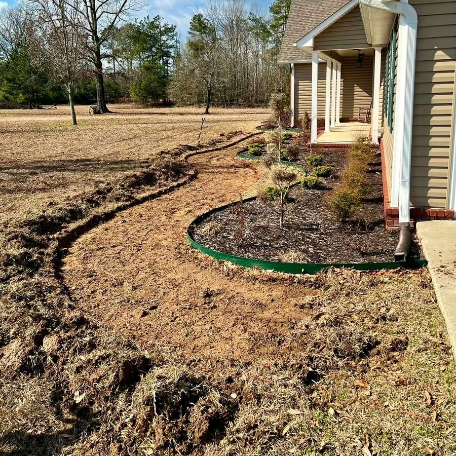 A curved bed outline dug into bare ground along the side of a house