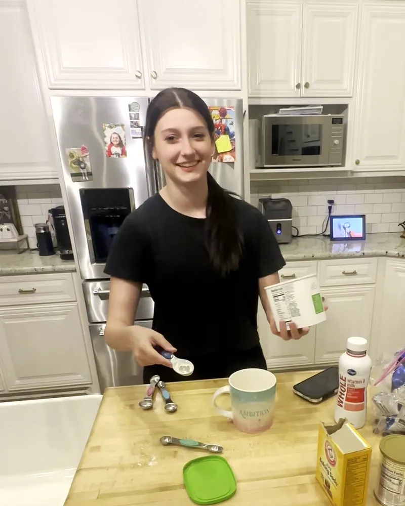 Anna Kate smiling at her kitchen counter with a measuring spoon, a mug and her baking ingredients