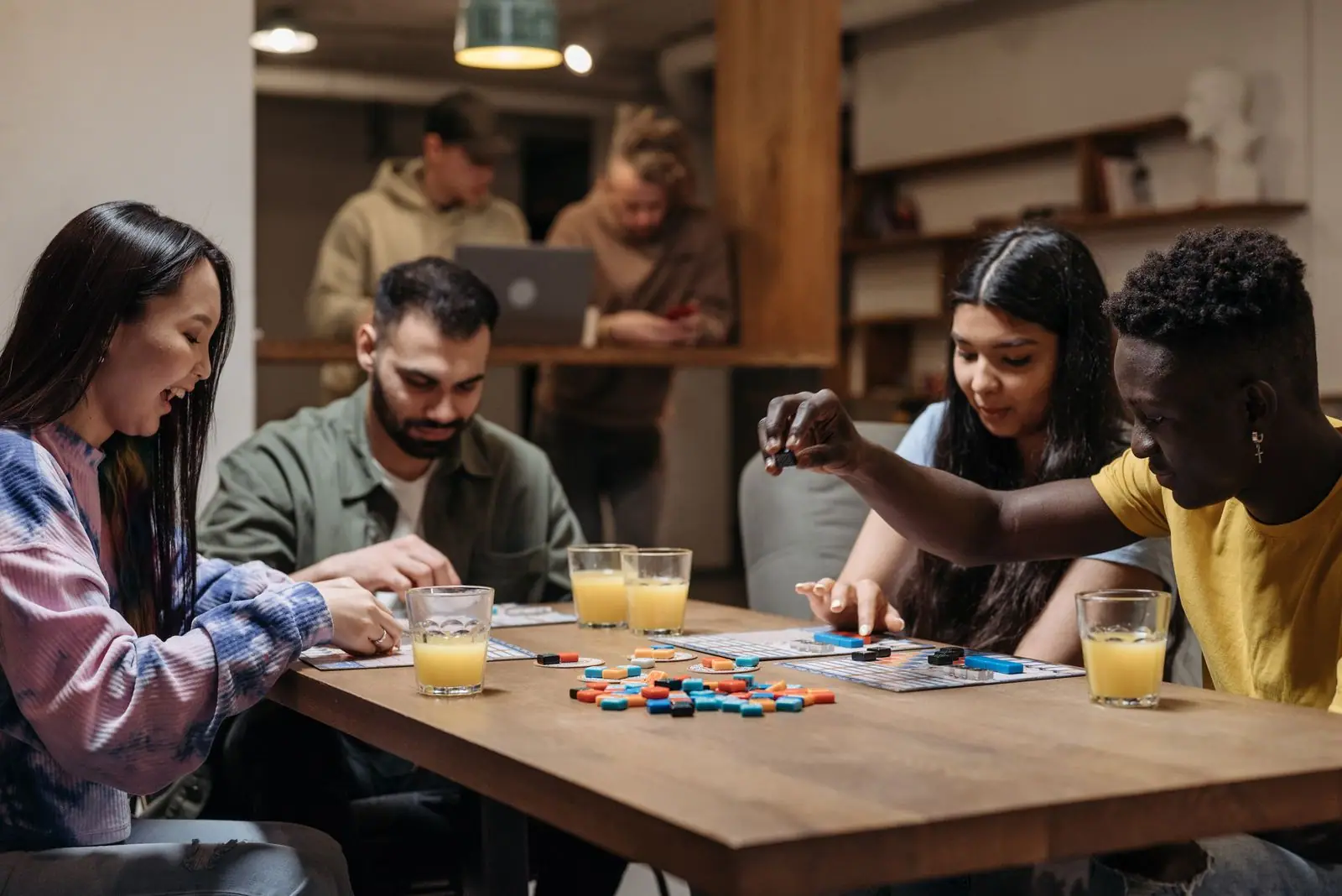 Four friends leaning over a board game at a wooden table